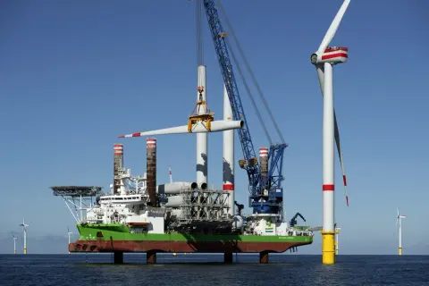 Ein Spezialschiff hebt eine Windradgondel an, um sie auf einem Turm zu montieren. Die Beine des Schiffes sind ausgefahren, um es zu jack up.