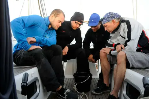 Vier Männer auf einem Boot, die sich über etwas beugen. Sie scheinen die Seefahrt zu genießen und haben ihre "sea legs" gut im Griff.