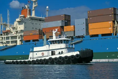 Ein kleiner Schlepper assistiert einem riesigen Containerschiff. Der Unterschied zwischen vessel und ship wird hier deutlich.