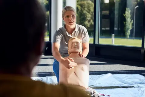 Frau zeigt an einer Übungspuppe die Herzmassage. Sie erklärt die korrekte Position für den Williamson Turn.