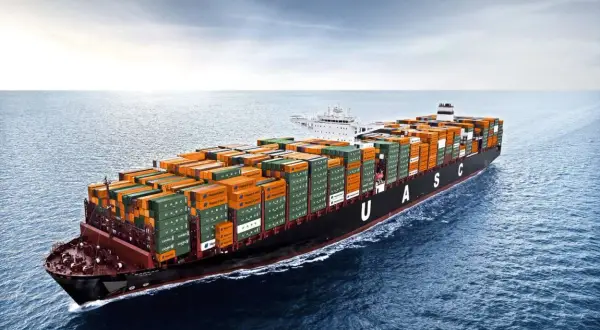 Ein riesiges Containerschiff mit orangefarbenen und grünen Frachtcontainern fährt auf dem Meer. Die UASC-Schriftzüge sind gut sichtbar. Die globale Logistik ist auf dem Weg, die Transitzeit zu optimieren.