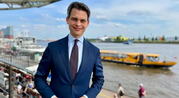 Ein Mann im Anzug steht am Hafen. Im Hintergrund fährt ein gelbes Ausflugsboot. Er ist ein port agent, der die Schiffe im Blick hat.