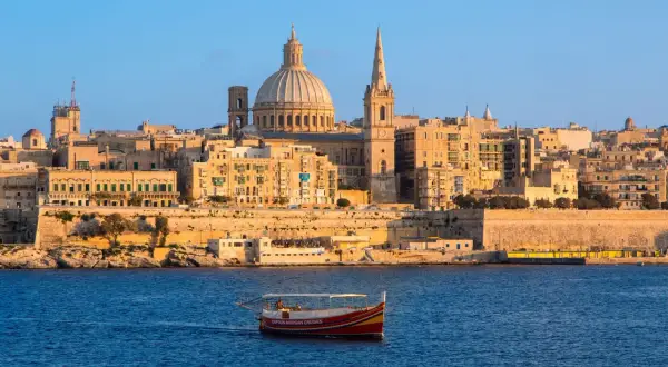 Ein Boot fährt im malta port vor der Skyline von Valletta mit der Kuppel der St. Paul's Cathedral.