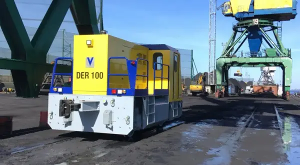 Gelbe Lokomotive "DER 100" im Riga Port, bereit für den Kohletransport unter großen Kränen.