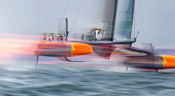 Schnelles Katamaran-Segelboot mit Besatzung, das über das Wasser gleitet. Die orangefarbenen Rümpfe und die Segel sind durch die Bewegung verschwommen, was die Geschwindigkeit des Sail GP-Rennens zeigt.
