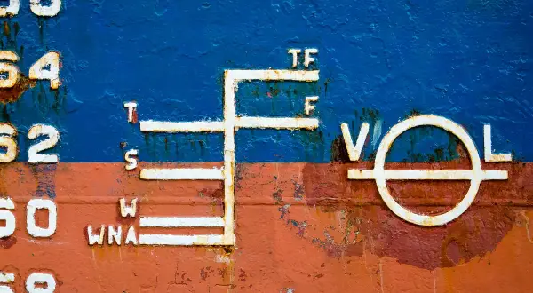Schiffsbord mit Markierungen, die die Tiefgangslinien (plimsoll line) anzeigen. Zahlen und Buchstaben wie 56, 54, 52, 50, 68, T, S, W, WNA, TF, F, V, O, L sind sichtbar.