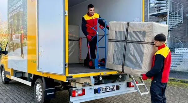 Zwei Männer laden ein großes Paket aus einem LKW. Ein Mann schiebt es mit einem Hubwagen, der andere trägt es. Maersk e-delivery macht es möglich.