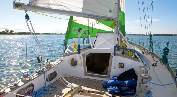 Segelboot mit grünen und weißen Segeln, die im Wind flattern. Die Website "wilfried-erdmann.de" ist auf dem Großsegel zu sehen.