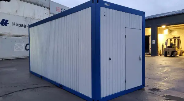 Ein blauer und weißer Container steht auf einem Container-Depot. Im Hintergrund sind weitere Container und ein Gabelstapler zu sehen.
