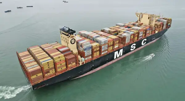 Die MSC Irina, ein riesiges Containerschiff, transportiert Fracht über das Meer. Ein kleines Beiboot fährt nebenher.