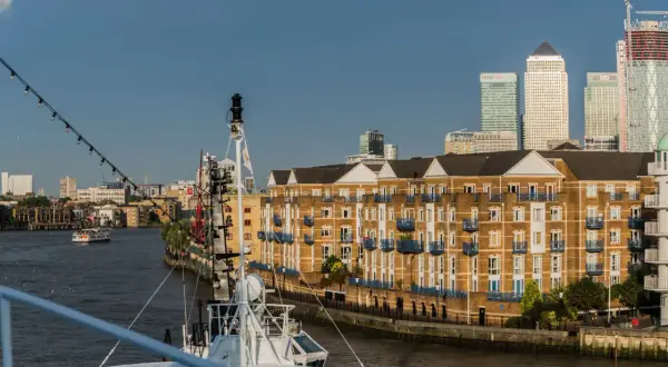 Blick auf den London Harbour mit modernen Hochhäusern und einem Flussufer mit Backsteinbauten. Ein Schiff liegt im Vordergrund.