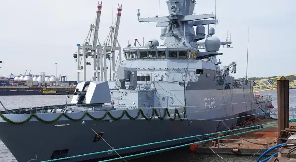 Graue corvette F266 im Hafen, mit Kranen und Containern im Hintergrund.