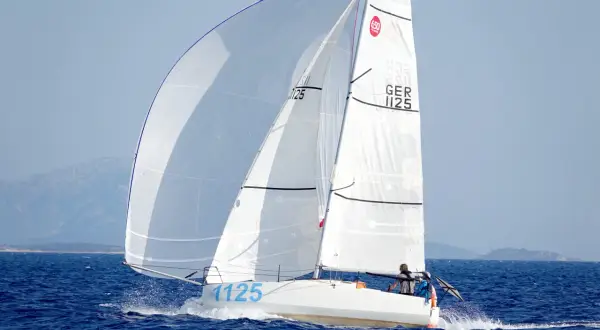 Segelboot mit zwei Personen an Bord, das auf dem Meer fährt. Die Segel sind weiß und mit der Nummer 1125 beschriftet. Dies ist ein Bild von einem Mini Transat Rennen.