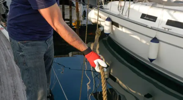 Mann mit roter Handschuh hält Seil an einem vertäuten Schiff.