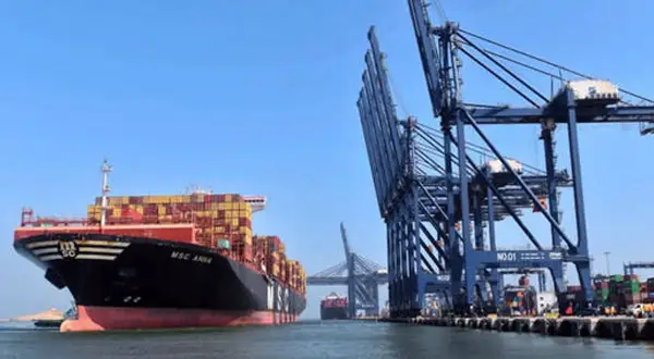 Ein riesiges Containerschiff liegt im Karachi Port vor Anker, während massive Kräne Container verladen.