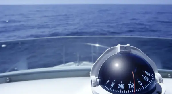 Kompass auf einem Boot zeigt die Richtung auf dem Meer. Teile des Bootes wie das Deck und die Windschutzscheibe sind sichtbar.