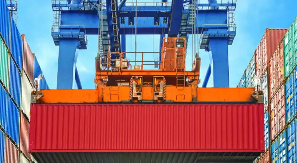 Ein roter Container wird von einem Kran gehoben. Die vgm methode 2 ist hier im Einsatz, um das Gewicht zu ermitteln.