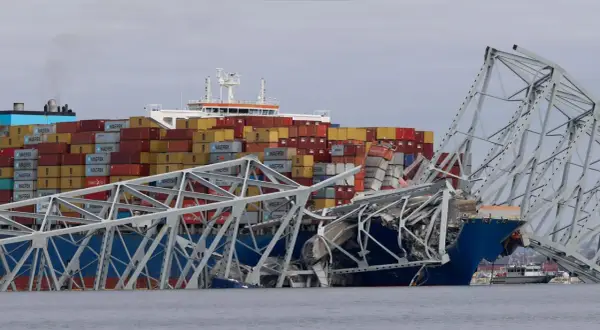 Ein Frachtschiff kollidiert mit einer Brücke, die in sich zusammenfällt. Container sind gestapelt, ein Zeichen für die globale Logistik, die in den US Ports stattfindet.