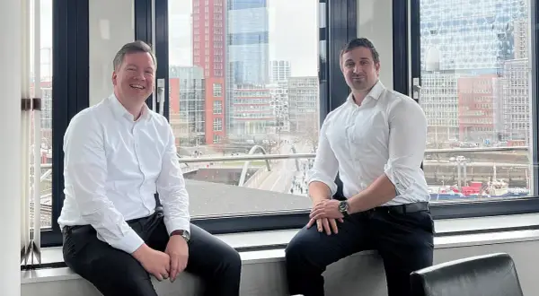 Zwei Männer, ein maritimer Anwalt und sein Kollege, sitzen vor einem Fenster mit Blick auf die Hamburger Hafencity.