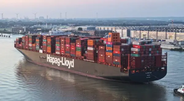 Ein riesiges Containerschiff, die "AL JMELIYAH", fährt auf einem Fluss, beladen mit bunten Frachtcontainern.