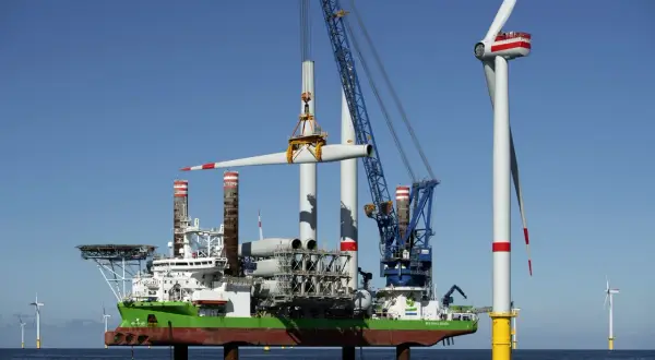 Ein Spezialschiff hebt eine Windradgondel an, um sie auf einem Turm zu montieren. Die Beine des Schiffes sind ausgefahren, um es zu jack up.