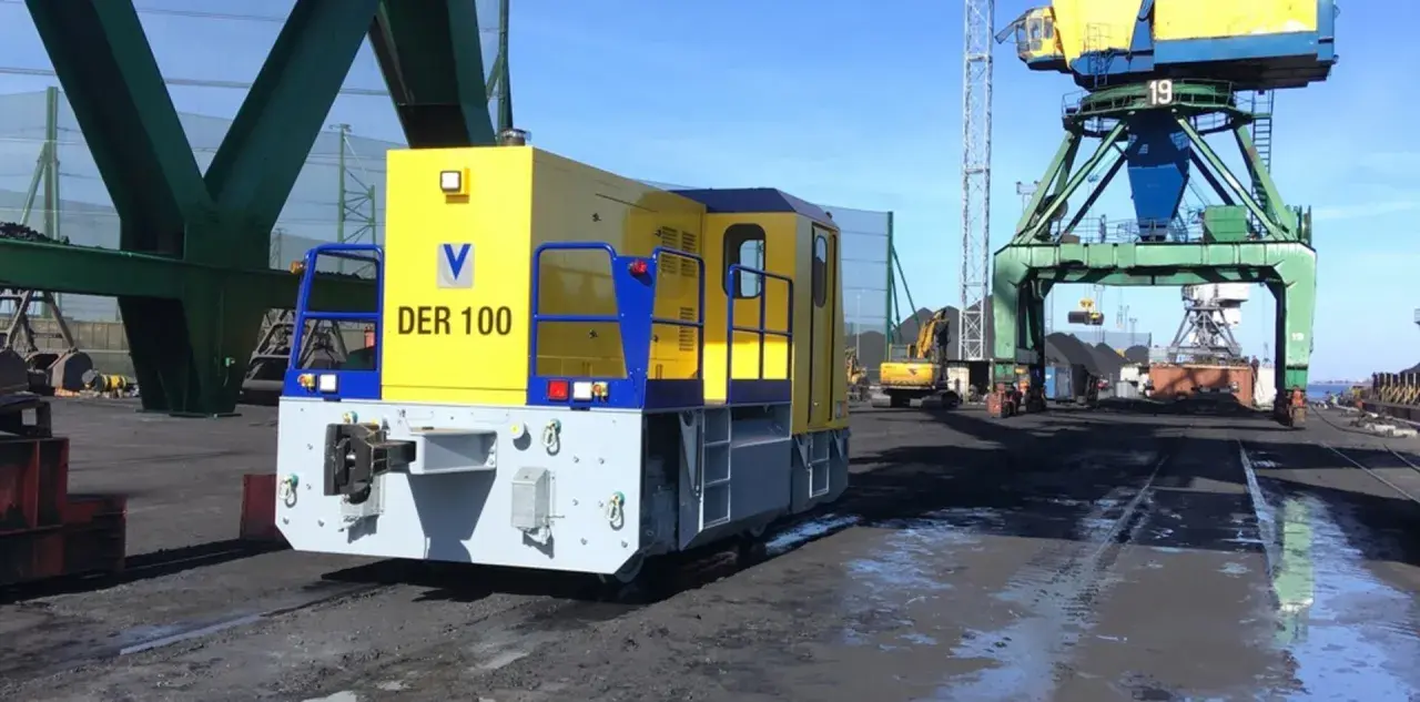 Gelbe Lokomotive "DER 100" im Riga Port, bereit für den Kohletransport unter großen Kränen.