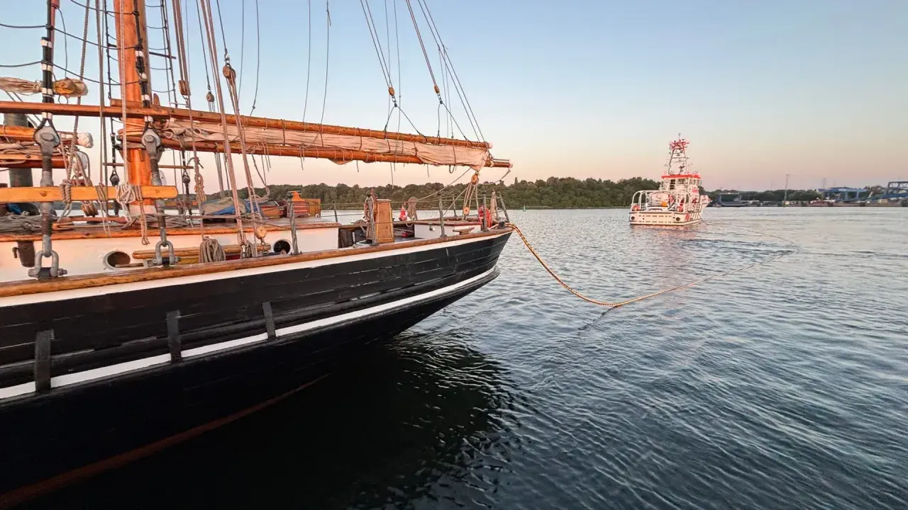 Ein majestätisches Albatros Segelschiff wird von einem Schlepper gezogen. Die Sonne geht unter und taucht das Wasser in ein warmes Licht.