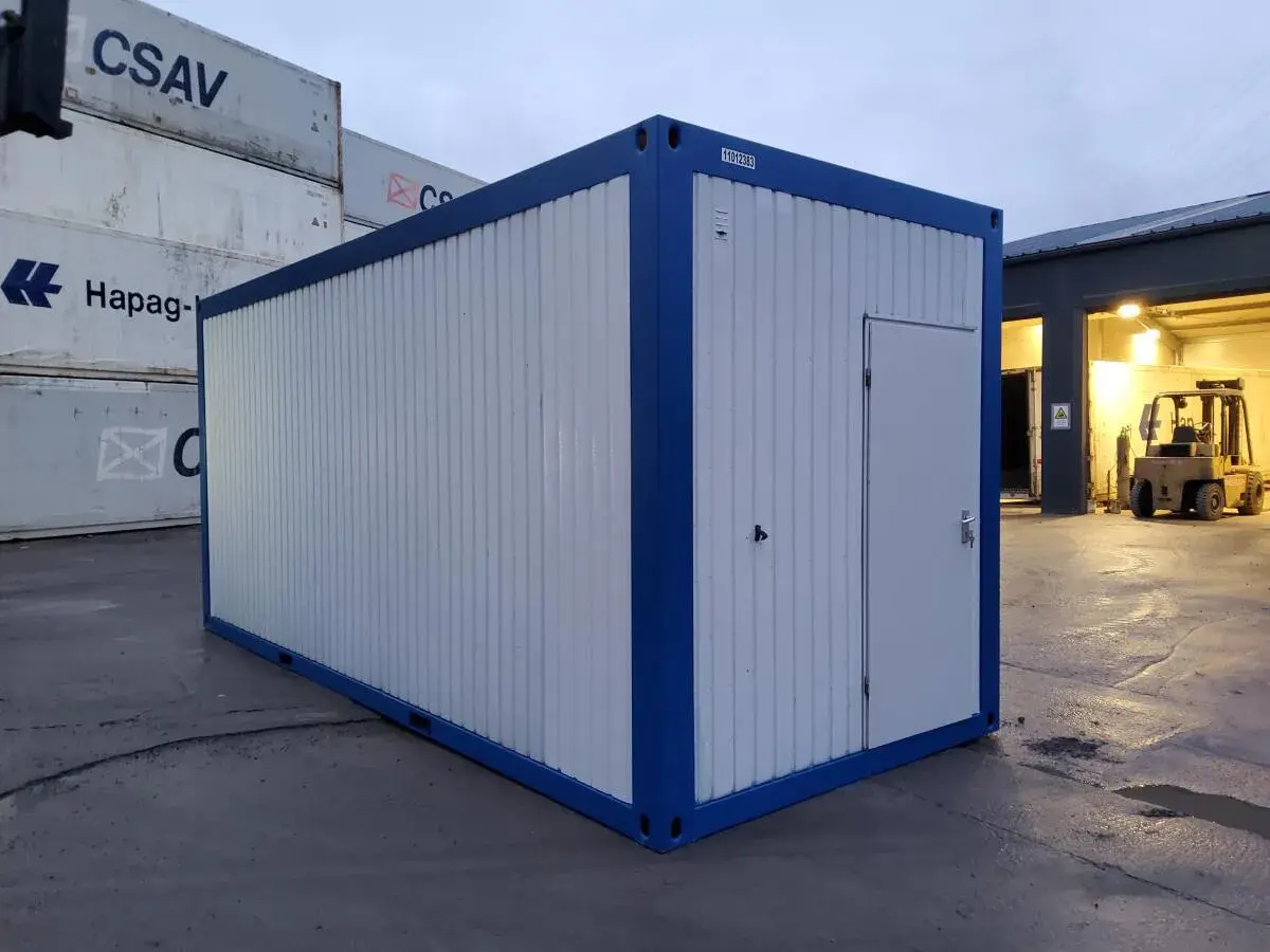 Ein blauer und weißer Container steht auf einem Container-Depot. Im Hintergrund sind weitere Container und ein Gabelstapler zu sehen.