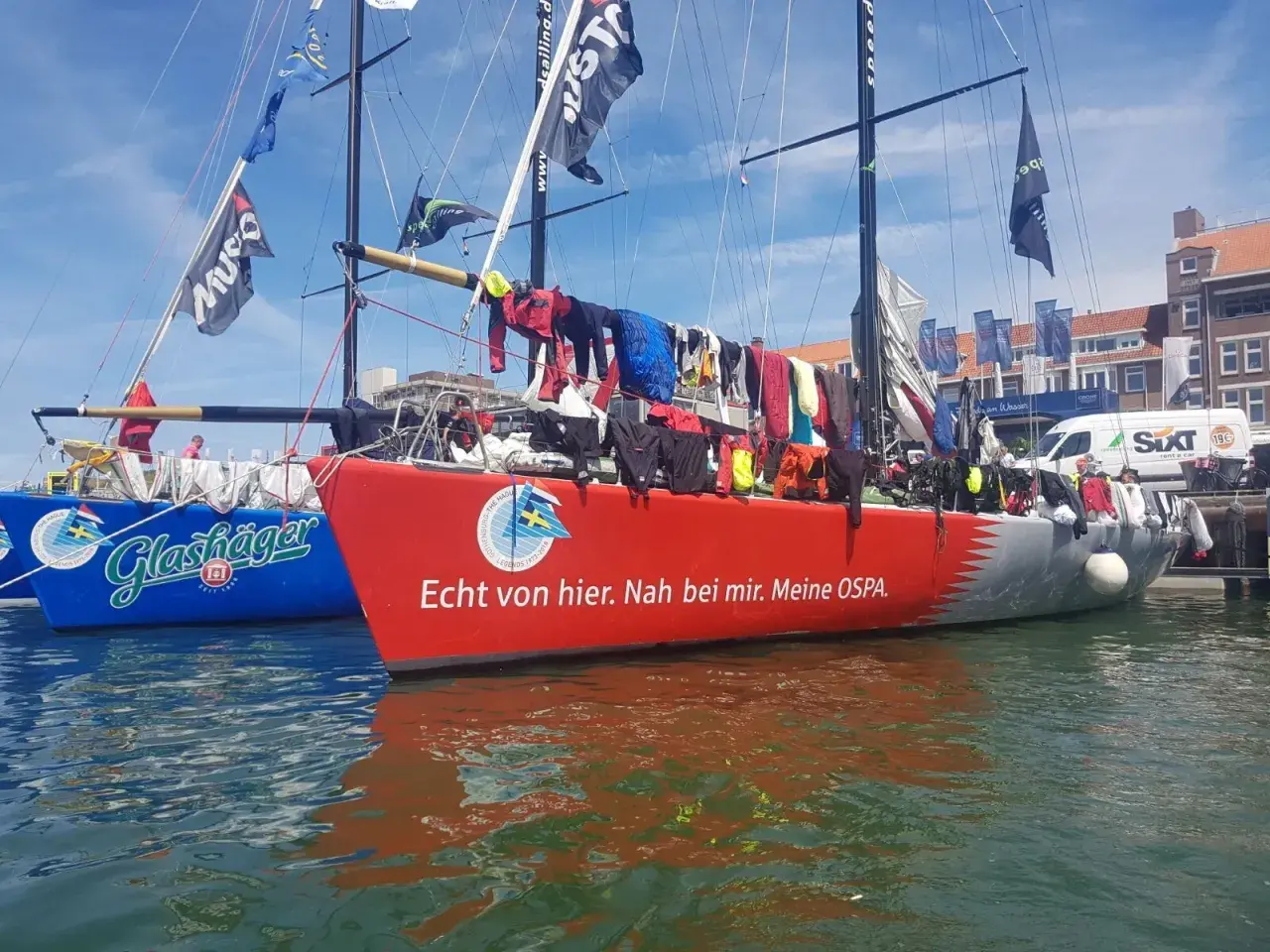 Segelboote im Hafen, Wäsche trocknet an Bord. Michael Illbrucks Boot "Meine OSPA" mit rotem Rumpf und Schriftzug.