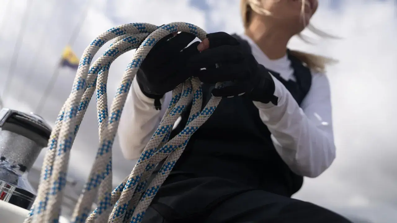 Seglerin mit Handschuhen hält Tauwerk, das für die wichtigsten Knoten auf einem Boot unerlässlich ist.