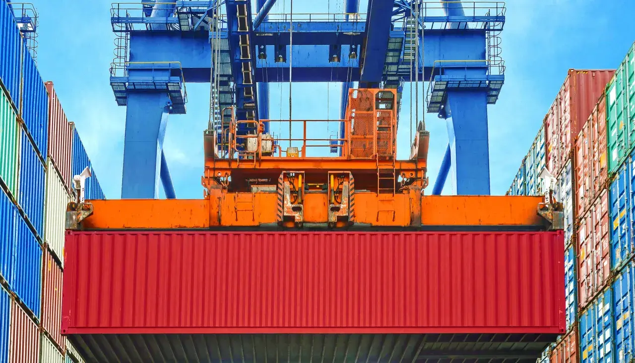 Ein roter Container wird von einem Kran gehoben. Die vgm methode 2 ist hier im Einsatz, um das Gewicht zu ermitteln.