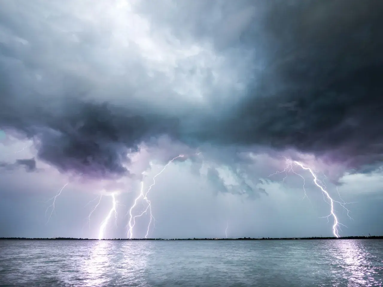 Ein heftiges Gewitter erhellt den Himmel über dem Meer. Blitze zucken, während ein einsames Segelboot auf dem Wasser treibt.