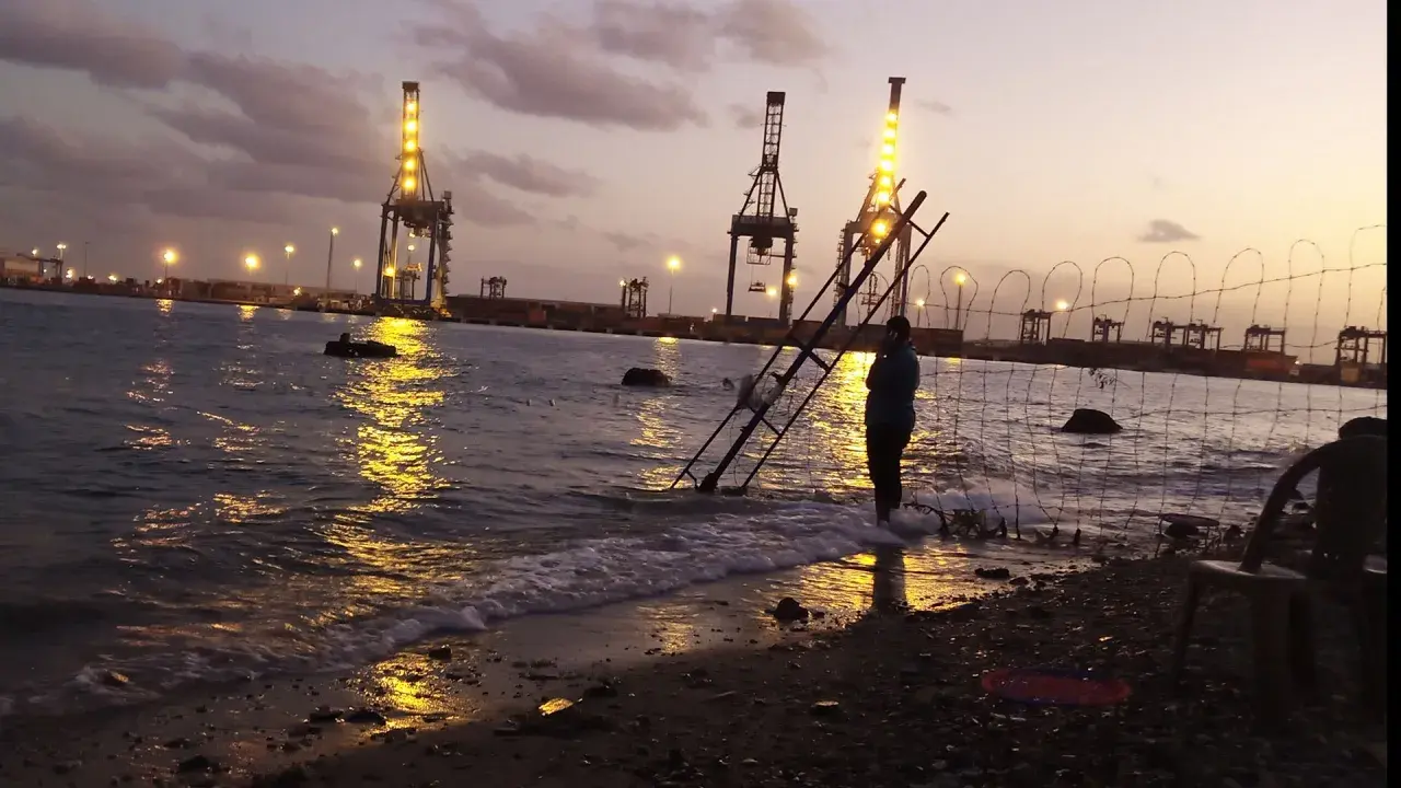 Abendstimmung am Hafen von Port Sudan. Kräne leuchten im Wasser, eine Person steht am Ufer.