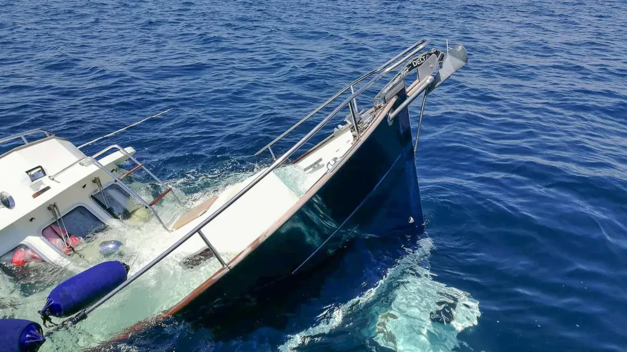 Ein sinkendes Boot neigt sich gefährlich im tiefblauen Meer. Rettungsringe und Fender treiben im Wasser.
