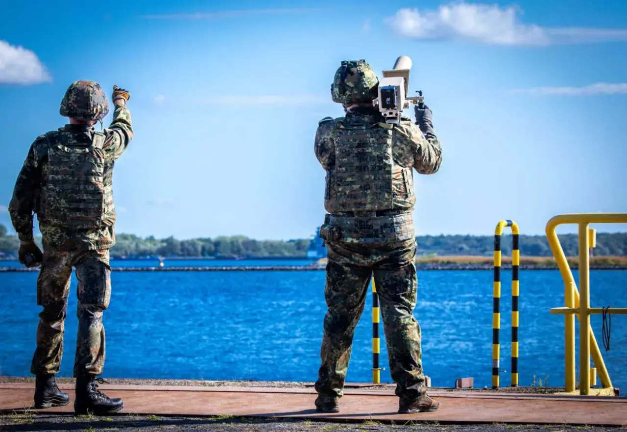 Zwei Soldaten sichern die Küste. Einer richtet eine Waffe, der andere hält ein Gerät. Maritime security in Aktion.