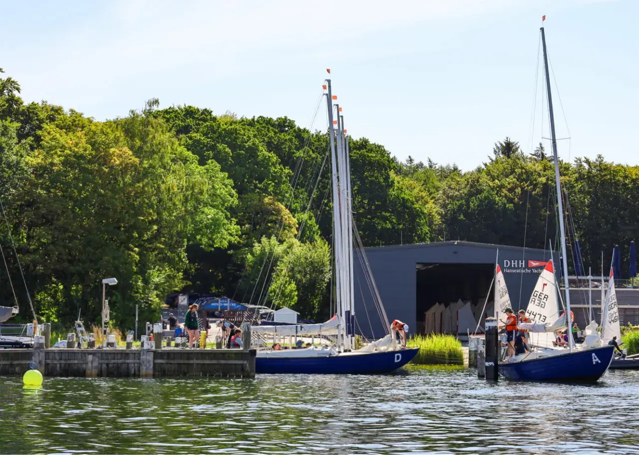 Segelboote am Steg der hanseatischen Yachtschule. Junge Segler üben auf dem Wasser.
