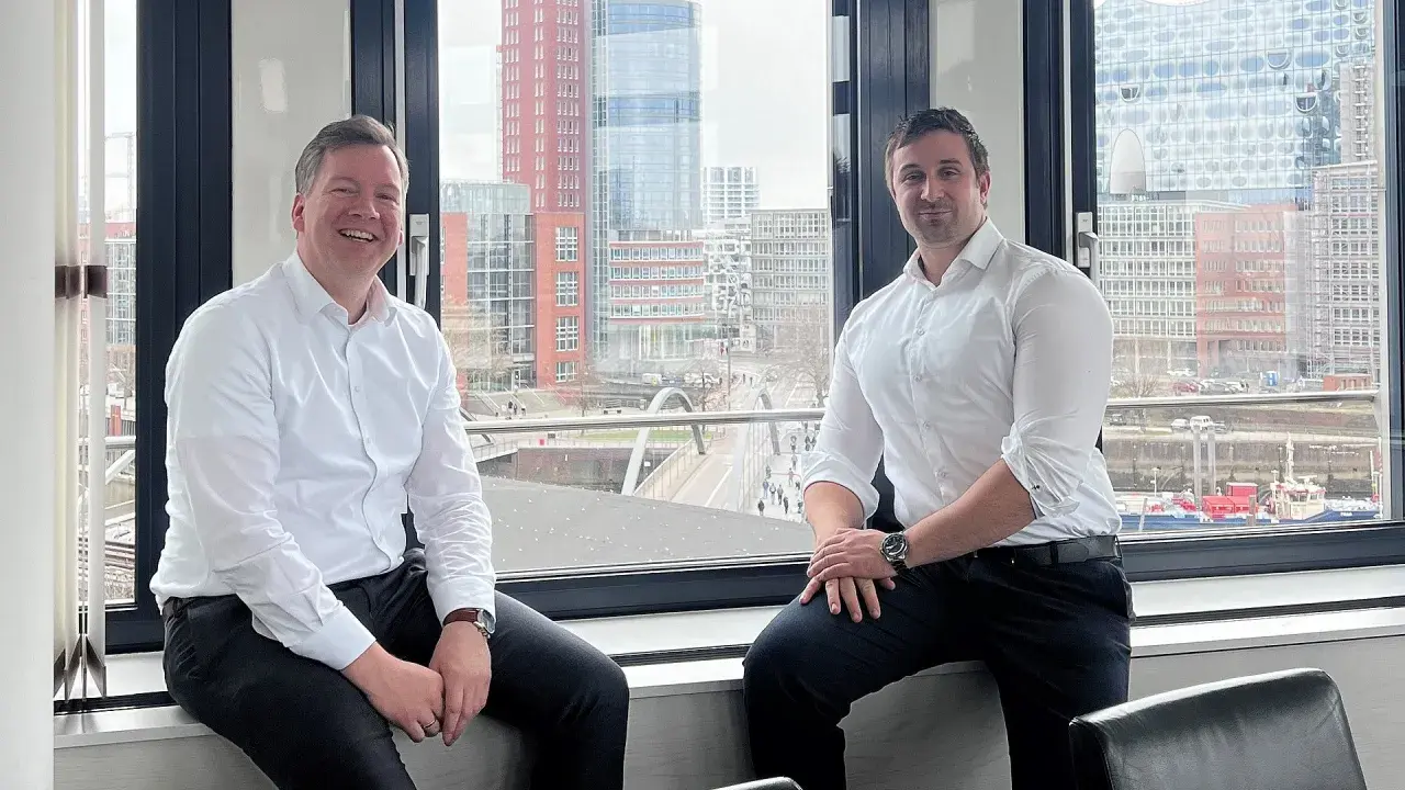 Zwei Männer, ein maritimer Anwalt und sein Kollege, sitzen vor einem Fenster mit Blick auf die Hamburger Hafencity.