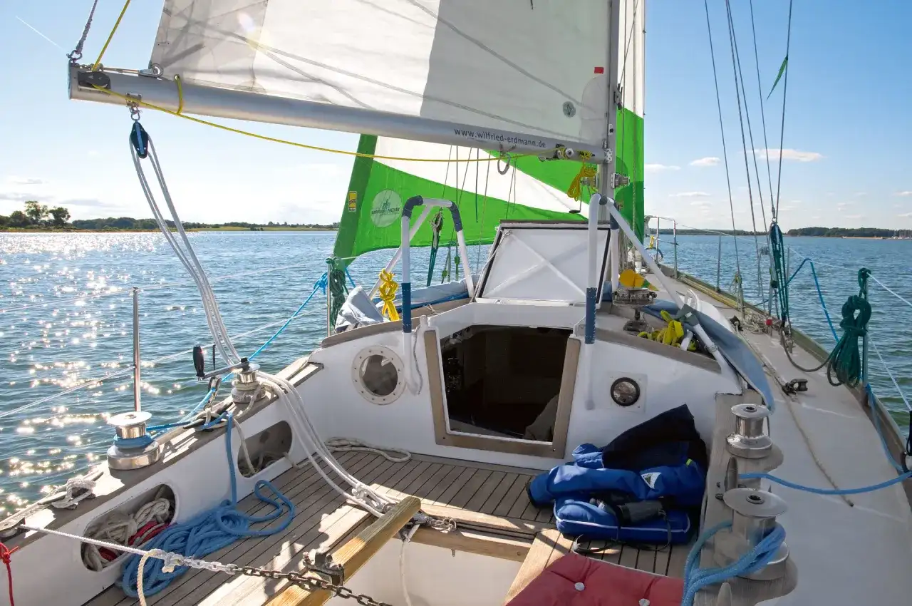 Segelboot mit grünen und weißen Segeln, die im Wind flattern. Die Website "wilfried-erdmann.de" ist auf dem Großsegel zu sehen.