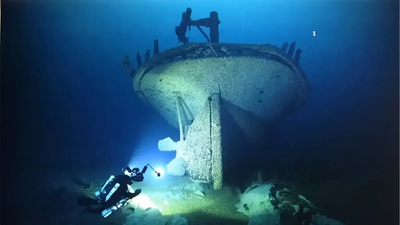 Ein Taucher erkundet einen gesunkenen Schiff-Wrack, dessen Heck im blauen Wasser aufragt.