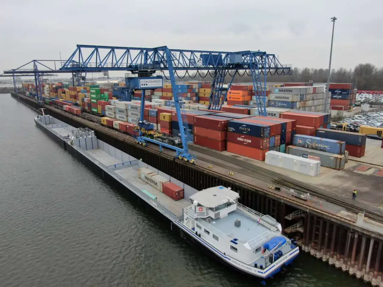 Ein Portagent &uuml;berwacht das Be- und Entladen von Containern auf ein Schiff und Z&uuml;ge in einem gesch&auml;ftigen Containerhafen.