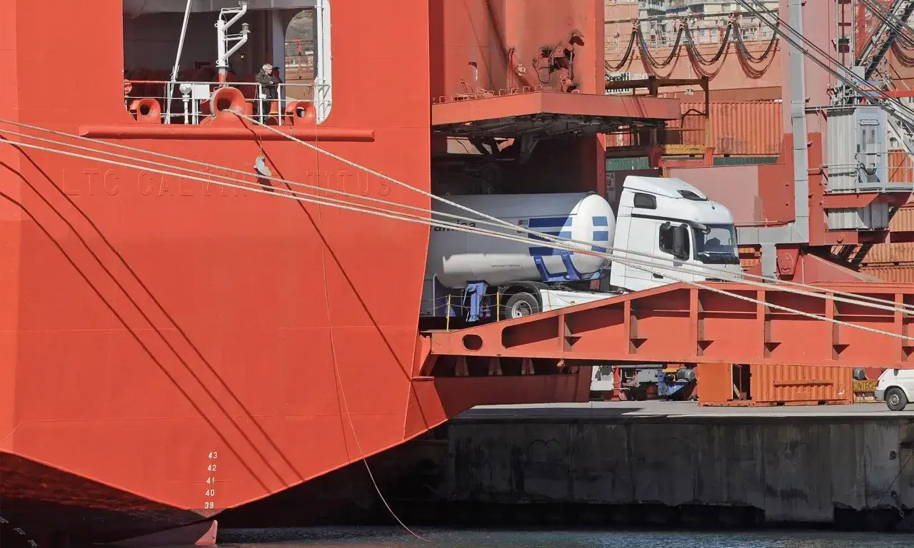 Ein wei&szlig;er Tanklastwagen wird per roll on roll off in einen gro&szlig;en roten Frachter geladen.