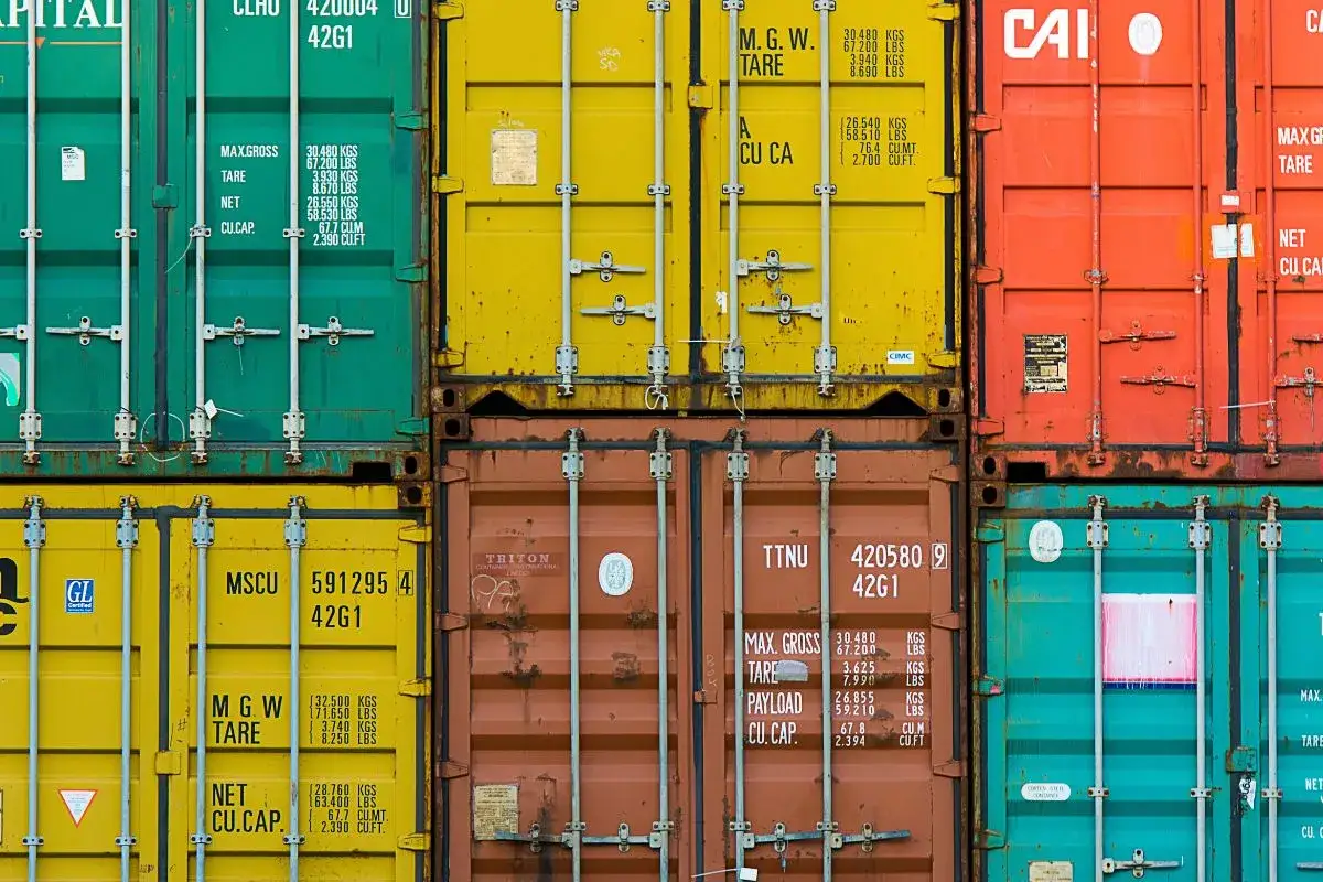 Gestapelte Container in Grün, Gelb, Orange und Blau. Ein gelber Container zeigt die Nummer MSCU 591295 42G1.