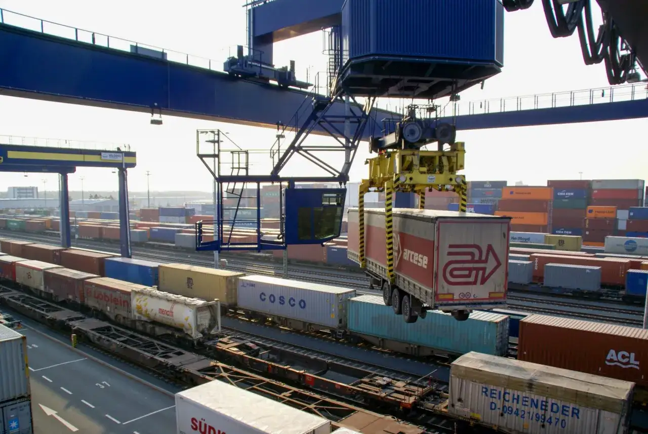 Ein Kran hebt einen LKW-Anh&auml;nger auf einen G&uuml;terzug. Dies ist ein Beispiel f&uuml;r integrierte Logistik, die verschiedene Transportmittel kombiniert.