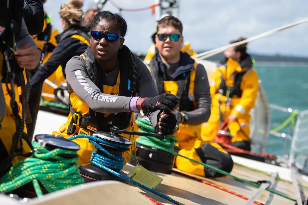 Segelteam in gelben Jacken bereitet sich auf ein spannendes ocean race vor. Sie bedienen die Winsch, um die Segel für den Wettkampf zu spannen.
