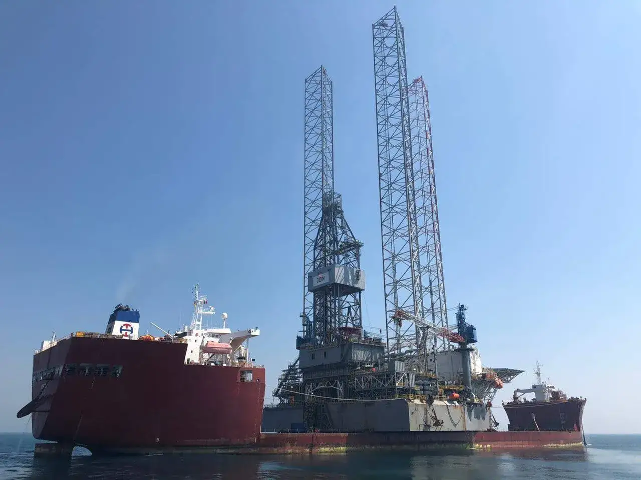 Ein riesiges Bohrplattformschiff, die Blue Marlin, wird von zwei Transportschiffen im Meer geschleppt.