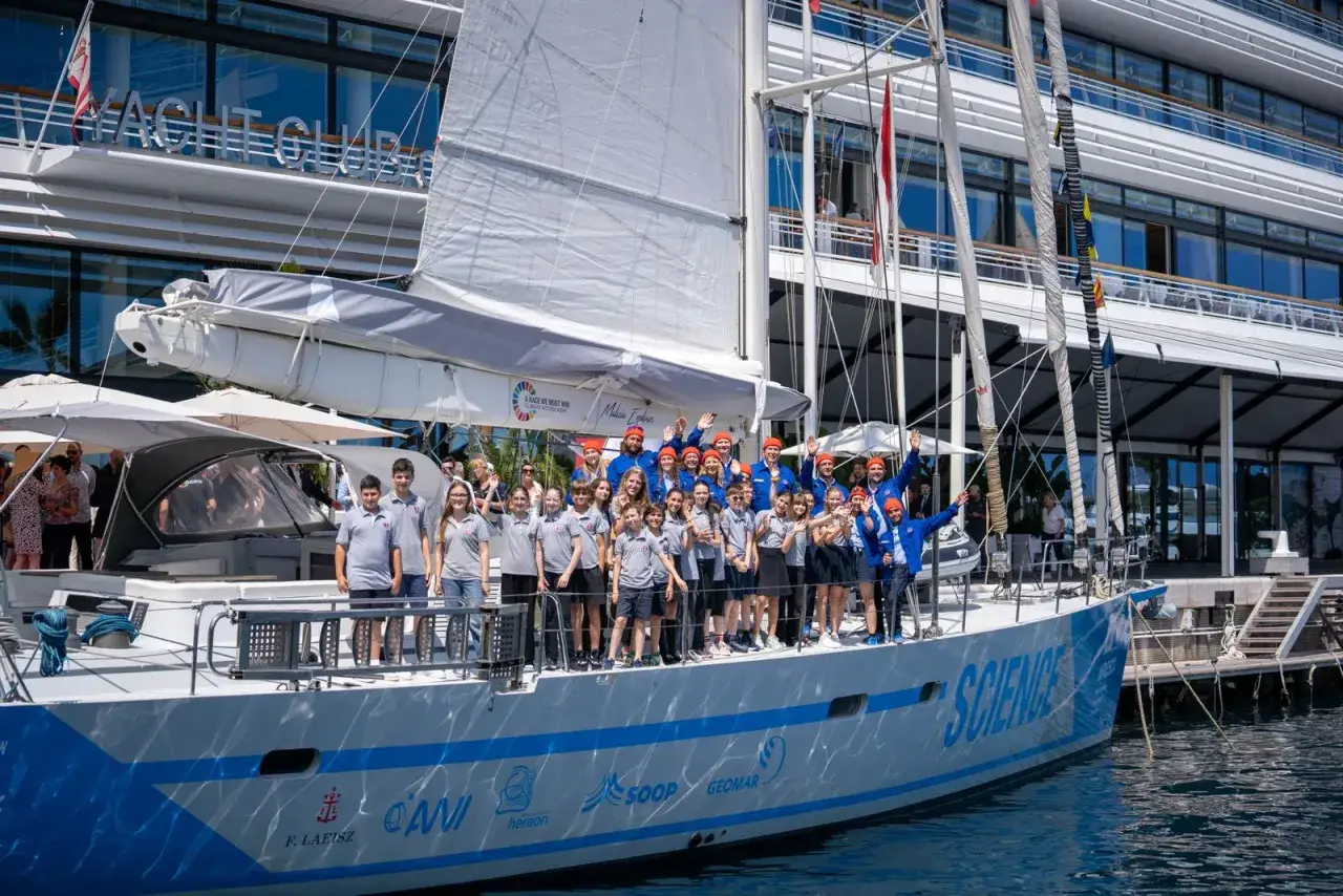 Eine Gruppe von Kindern und Erwachsenen steht auf einem Segelboot, das für die Malizia Ocean Race bereit ist.