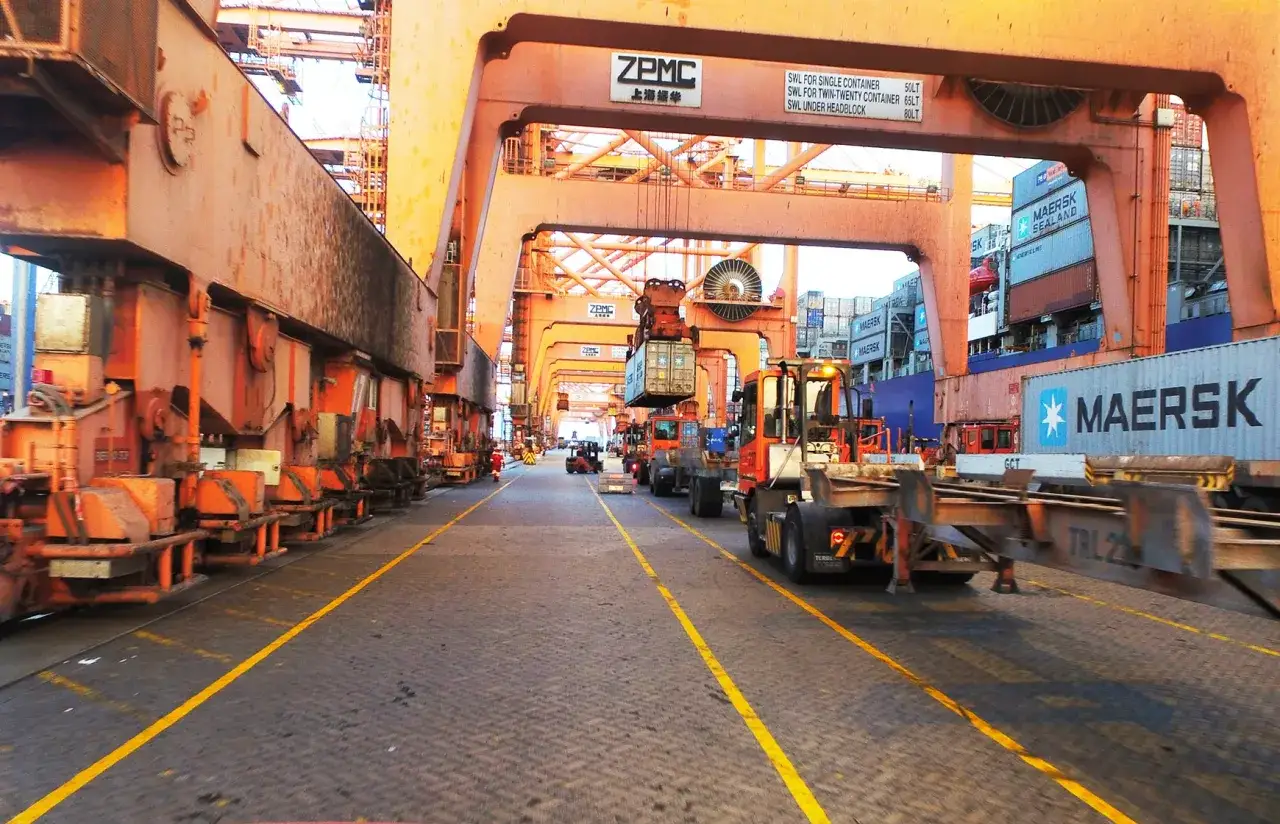Gro&szlig;e Kr&auml;ne und Container im Hafen von Salalah. Ein Gabelstapler transportiert einen Container, w&auml;hrend ein Schiff im Hintergrund beladen wird.