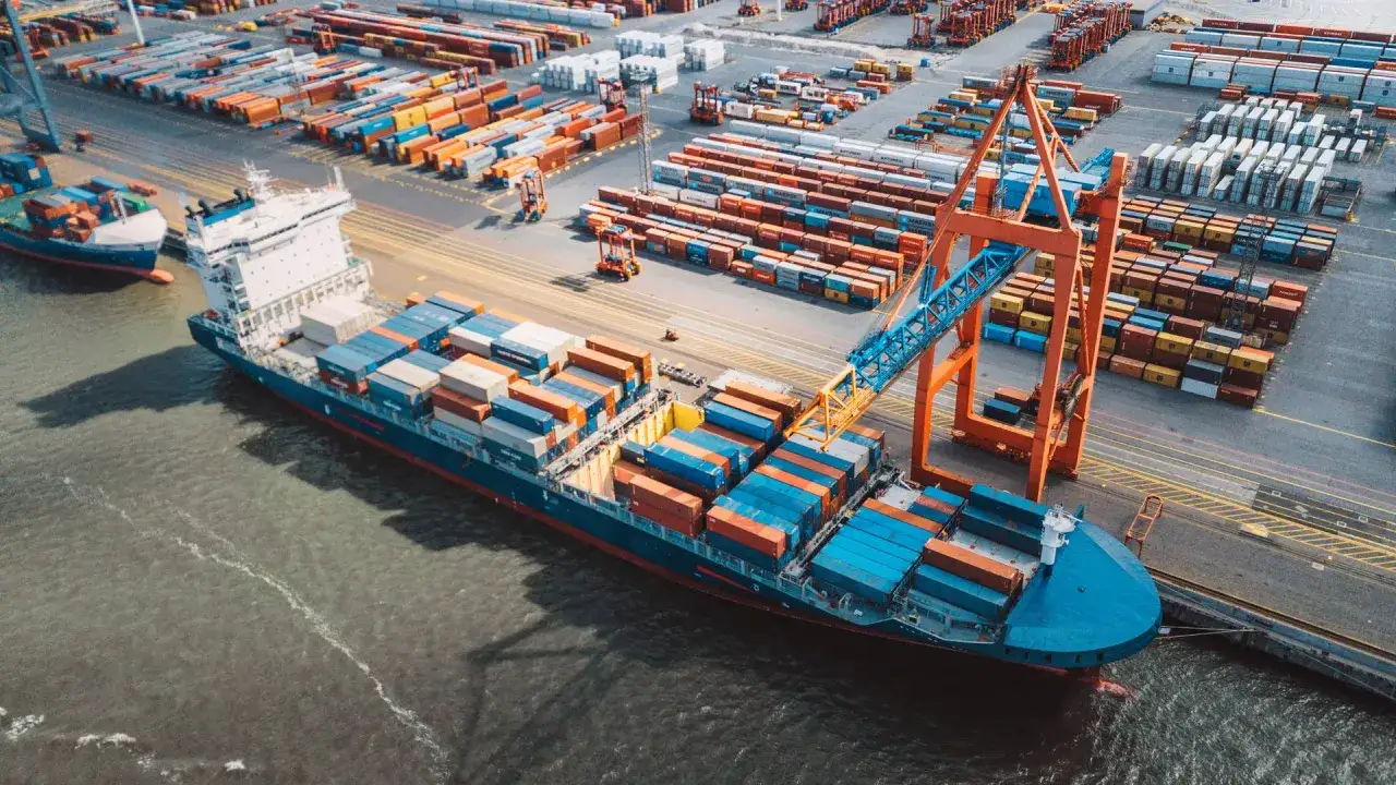 Ein Frachtschiff wird im Hafen entladen. Container stapeln sich auf dem Schiff und im Hintergrund, bereit für den Transport. Die ETA (geschätzte Ankunftszeit) ist entscheidend für die Logistik.
