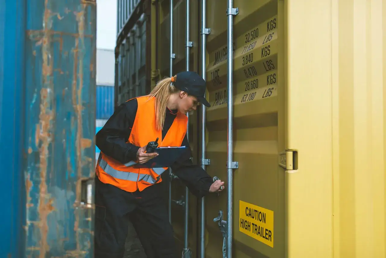 Frau in Warnweste prüft Containerdaten. Sie ist ein wichtiger Teil des Prozesses, der als clearing agent fungiert, um den Warenfluss zu sichern.