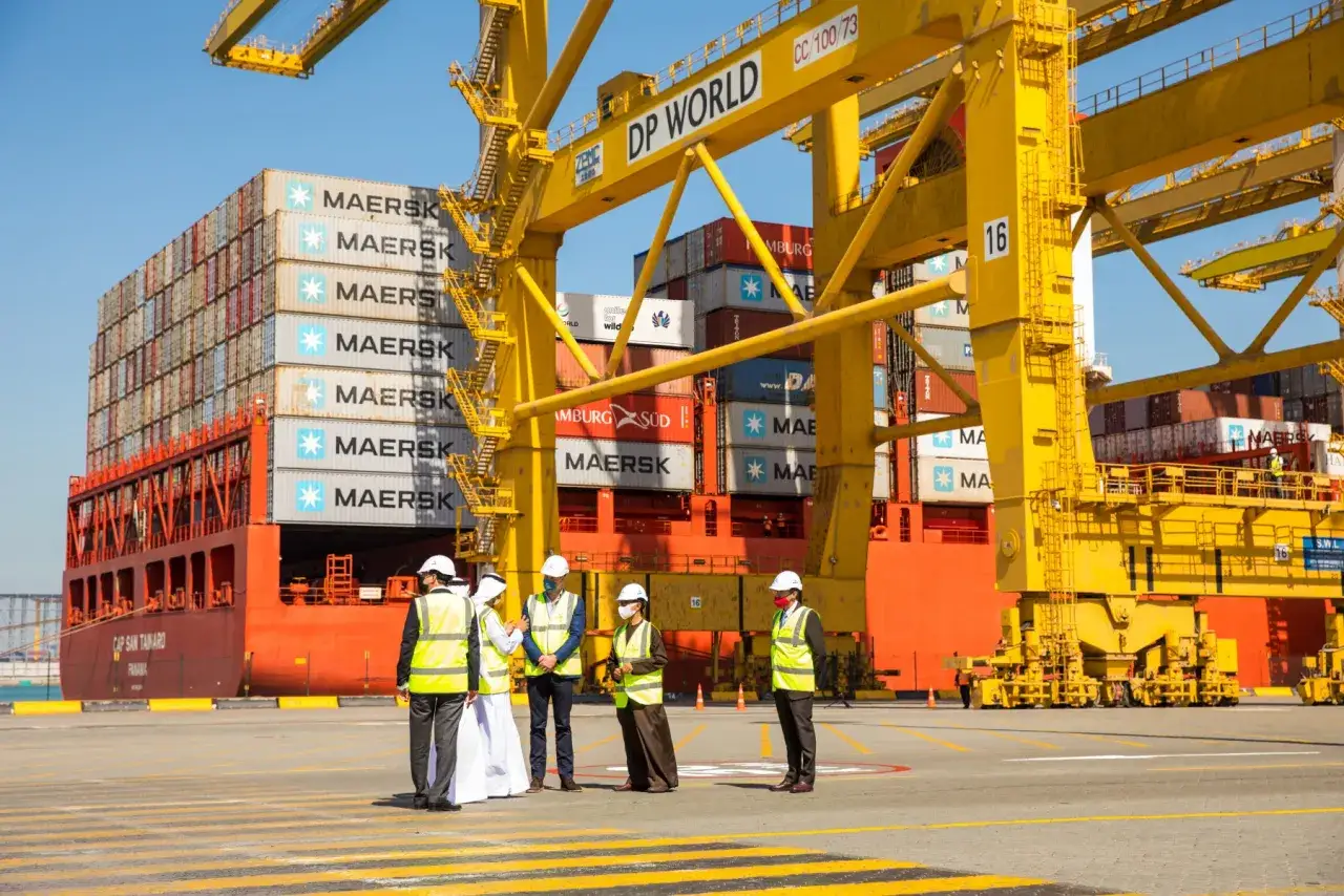 Mitarbeiter inspizieren einen riesigen Containerfrachter im Dubai Port, beladen mit Maersk-Containern, unter einem gelben DP World-Kran.